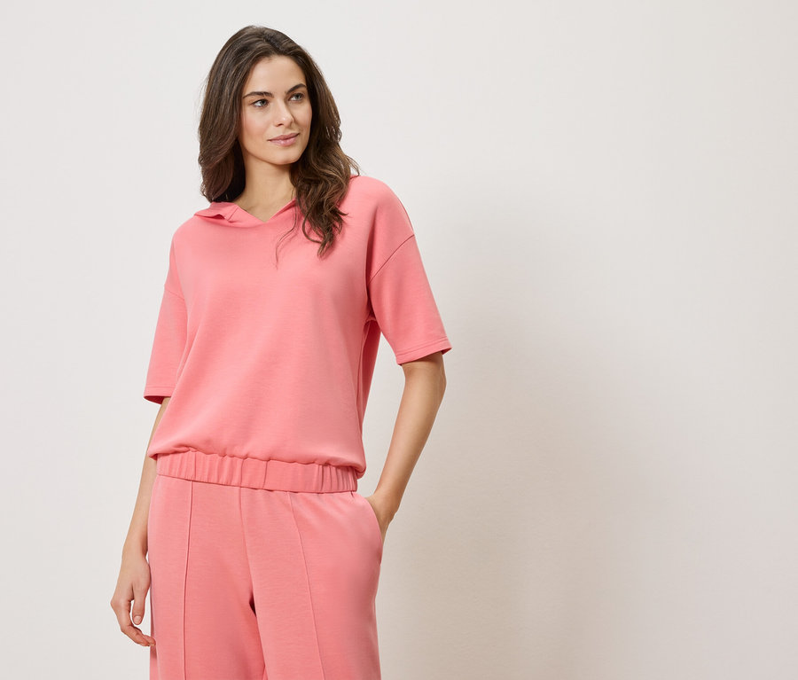 Kobieta ma na sobie różową bluzę z krótkim rękawem i kapturem oraz różowe spodnie.