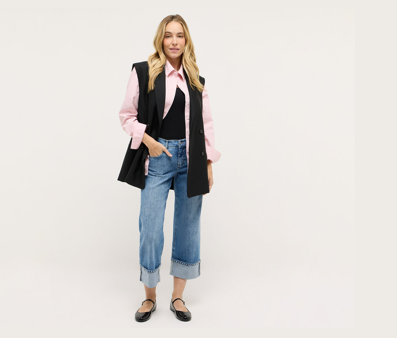 Kobieta w czarnej kamizelce, różowej koszuli, dżinsach i czarnych butach.