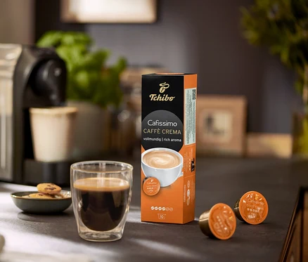 Ekspres do kawy z filiżanką kawy, ciasteczkami i opakowaniem kapsułek Cafissimo Caffe Crema.