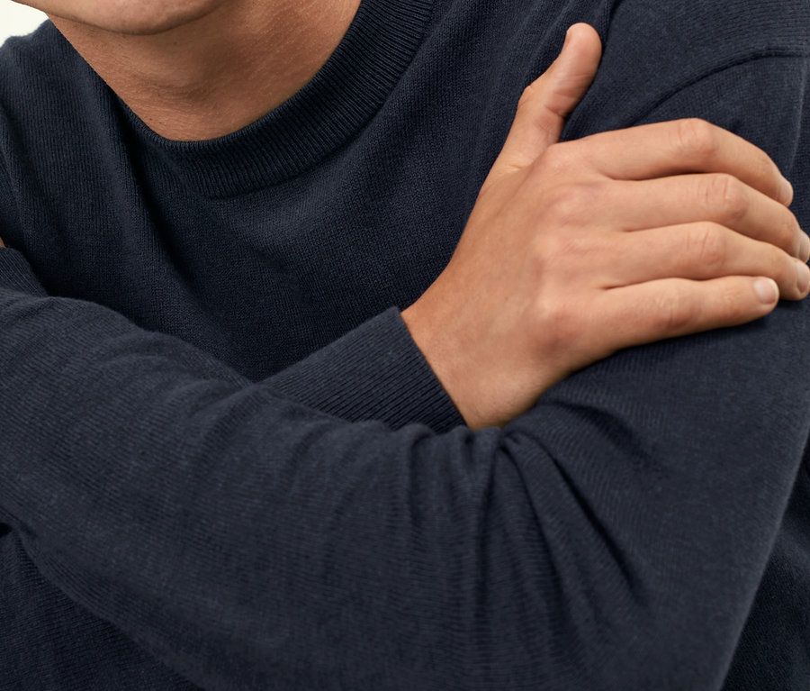 Mężczyzna ze skrzyżowanymi rękami ma na sobie granatowy sweter.