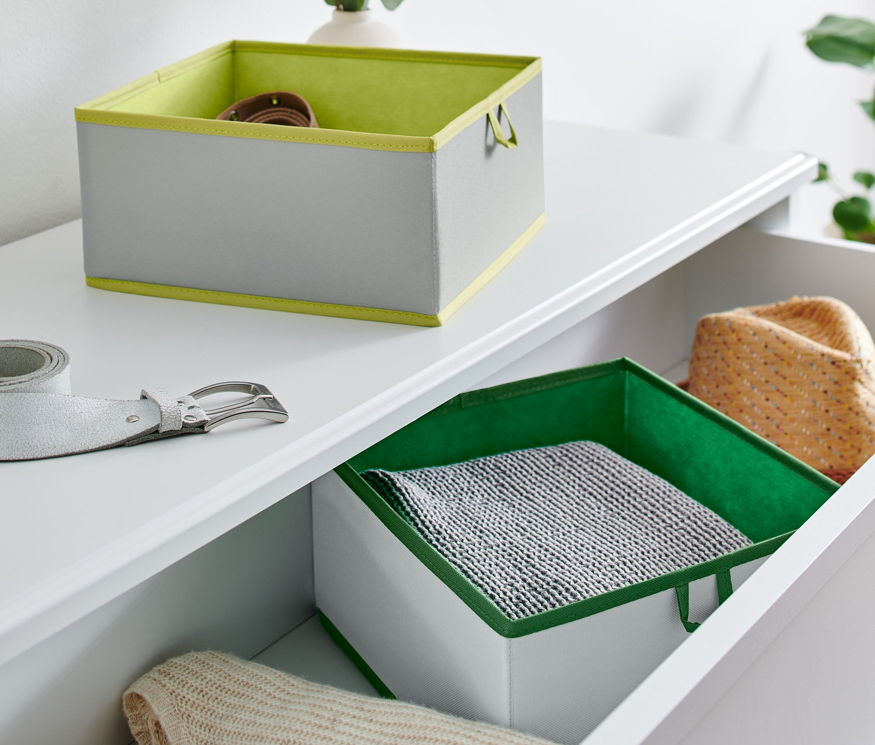 Na białej komodzie leżą dwa duże organizery do szuflad i srebrny pasek.