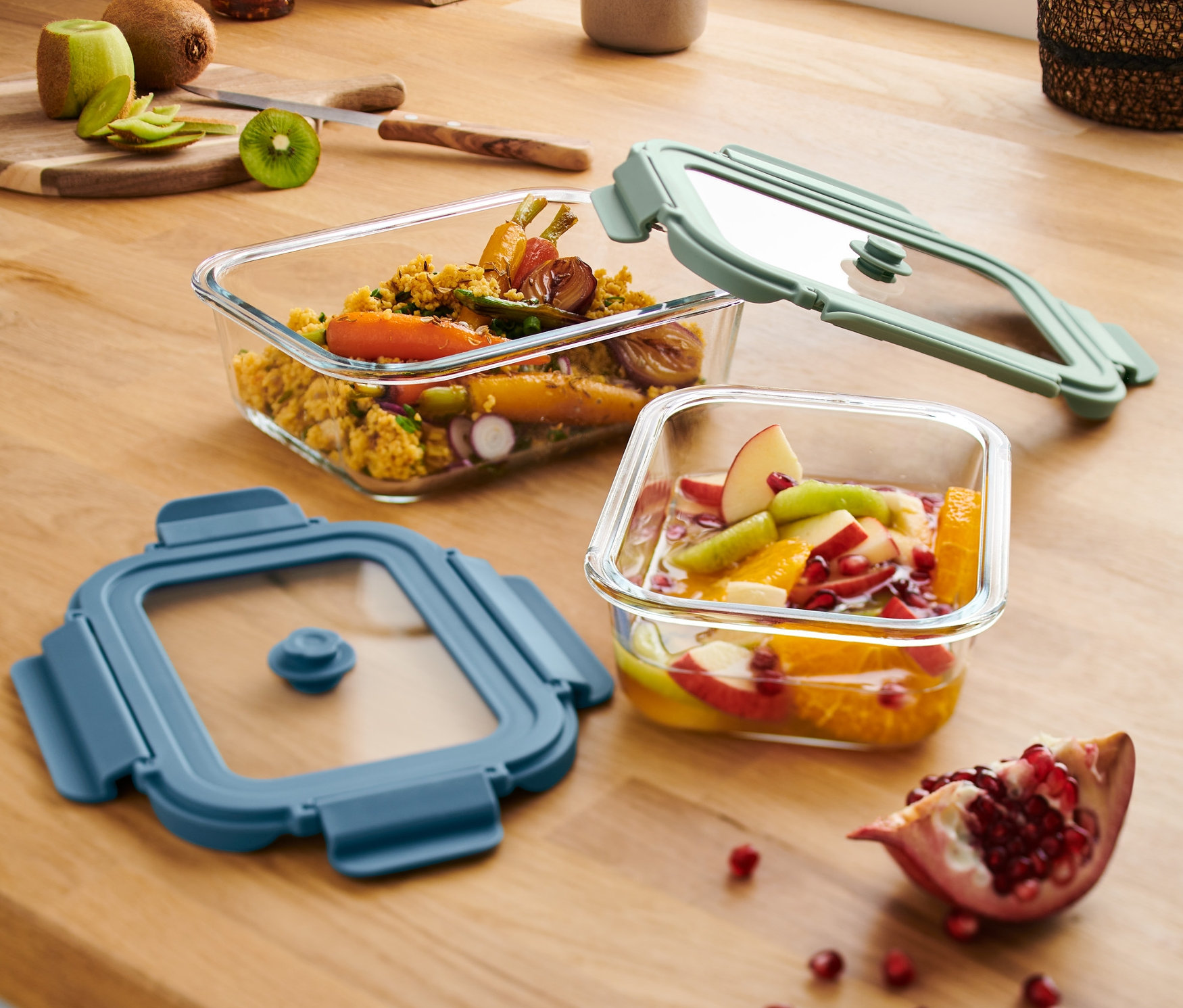 Dwie szklane formy do zapiekania z pokrywkami leżą na drewnianym blacie. Jedna forma jest pełna warzyw, druga owoców.