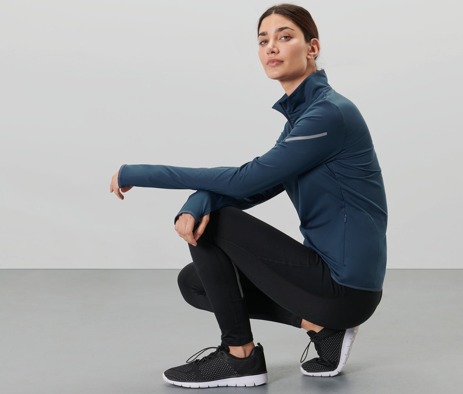 Kobieta w przysiadzie ma na sobie granatową termiczną bluzkę funkcyjną.