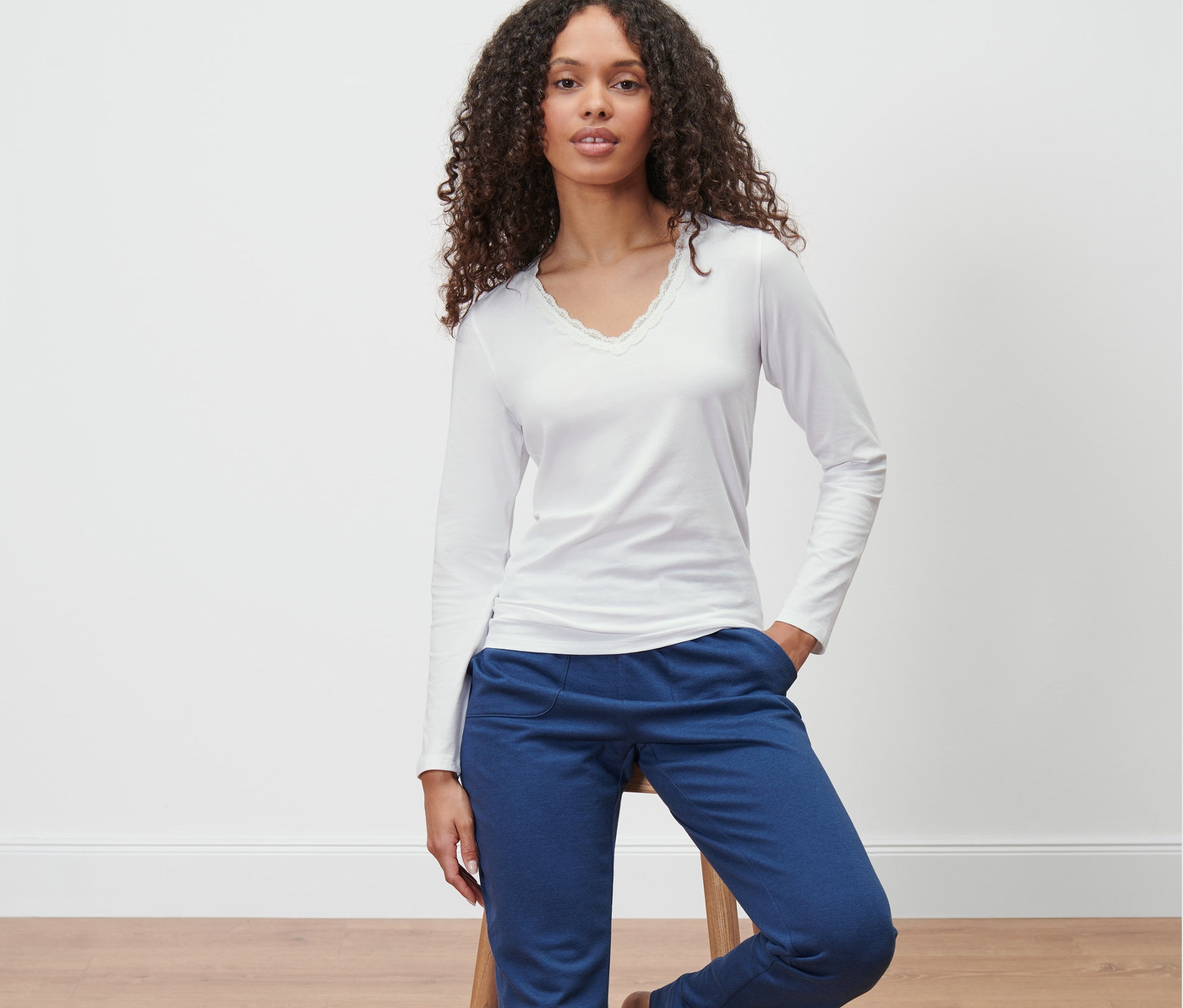 Kobieta siedzi na stołku w podkoszulce z długim rękawem i niebieskich spodniach.