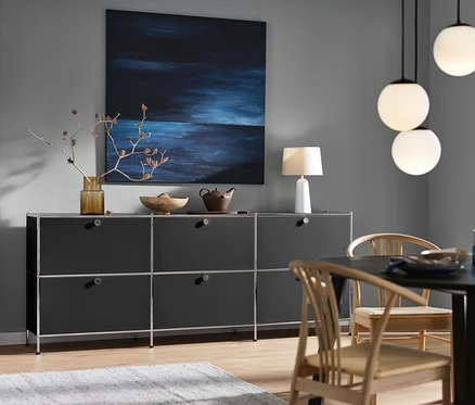 Czarna szafka typu sideboard »CN3« z 6 klapami, biała lampa stołowa z kloszem z tkaniny i lampa wisząca ze szklanymi kulami.