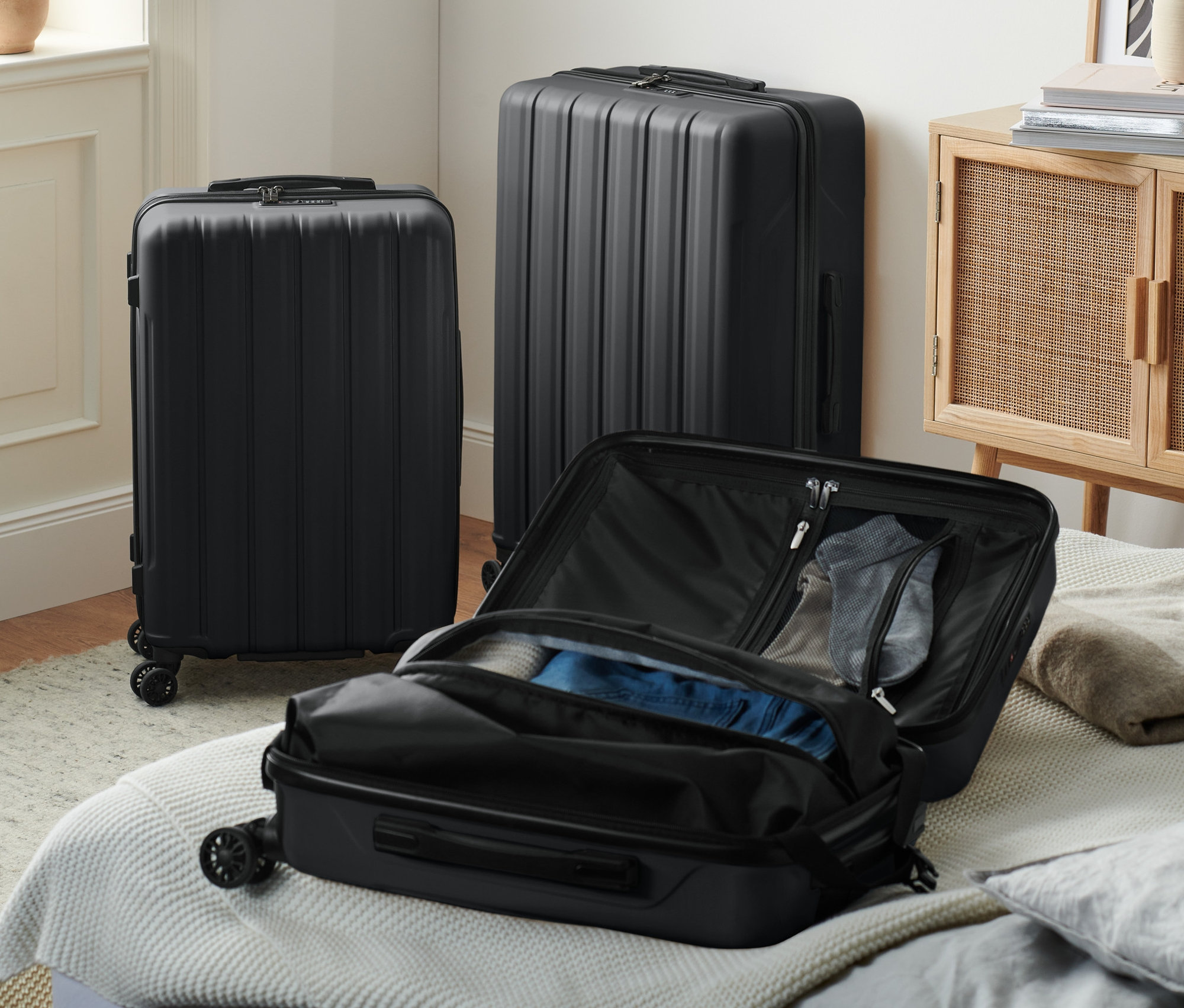 Trzy czarne twarde walizki, jedna otwarta na łóżku.
