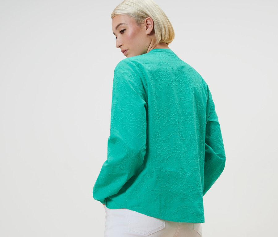 Kobieta pozuje w zielonej bluzce z haftem.
