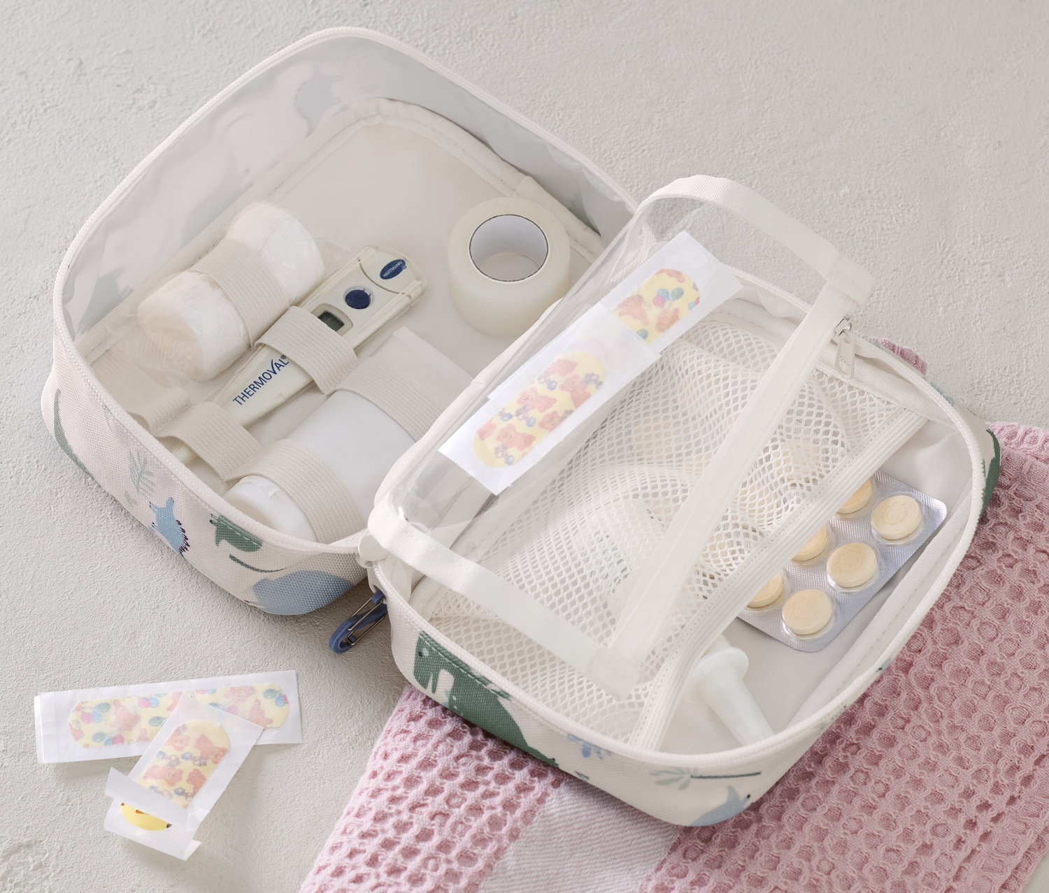 Otwarta torba na lekarstwa z zawartością i plastrami leży na różowym ręczniku.