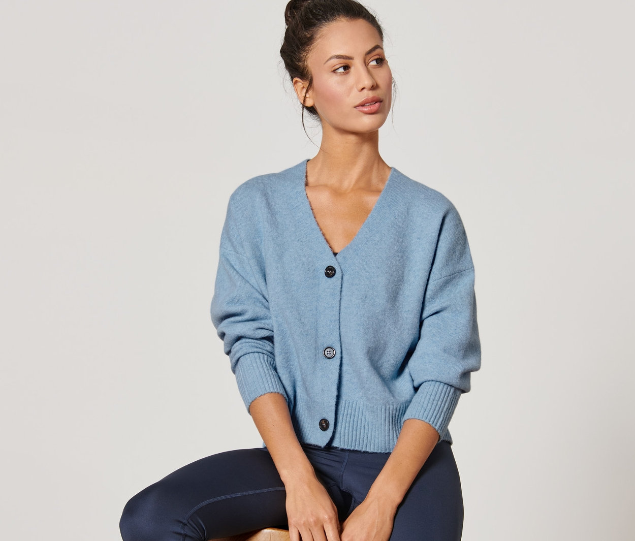 Kobieta siedzi na stołku, ubrana w niebieski kardigan o grubym splocie.