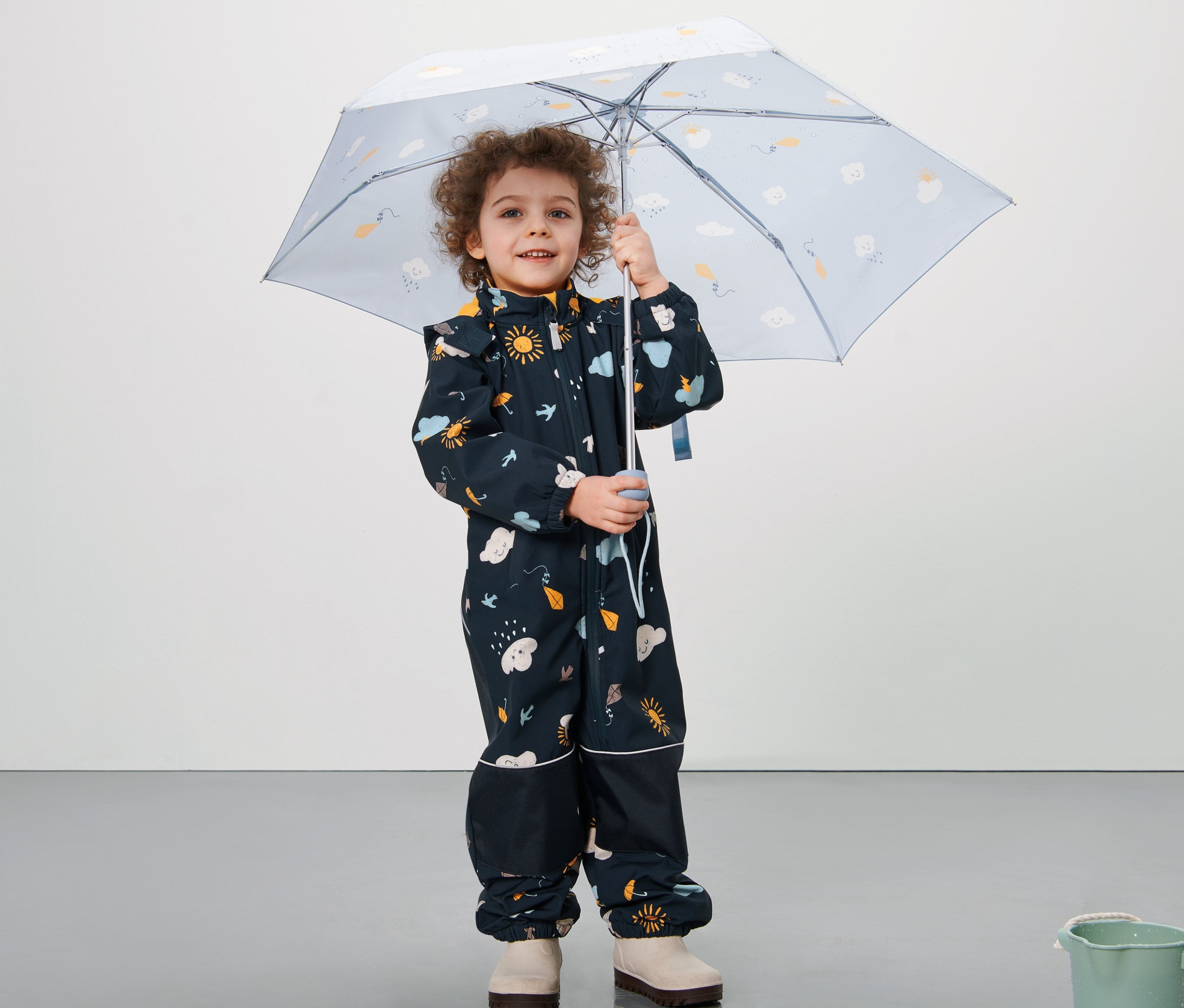 Chłopiec trzyma parasol i ma na sobie niebieski kombinezon softshell z nadrukiem na całej powierzchni.