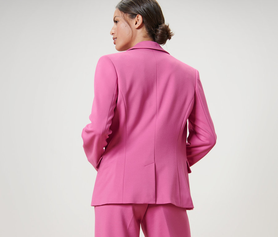 Kobieta w różowym komplecie, ma na sobie żakiet z dżerseju.