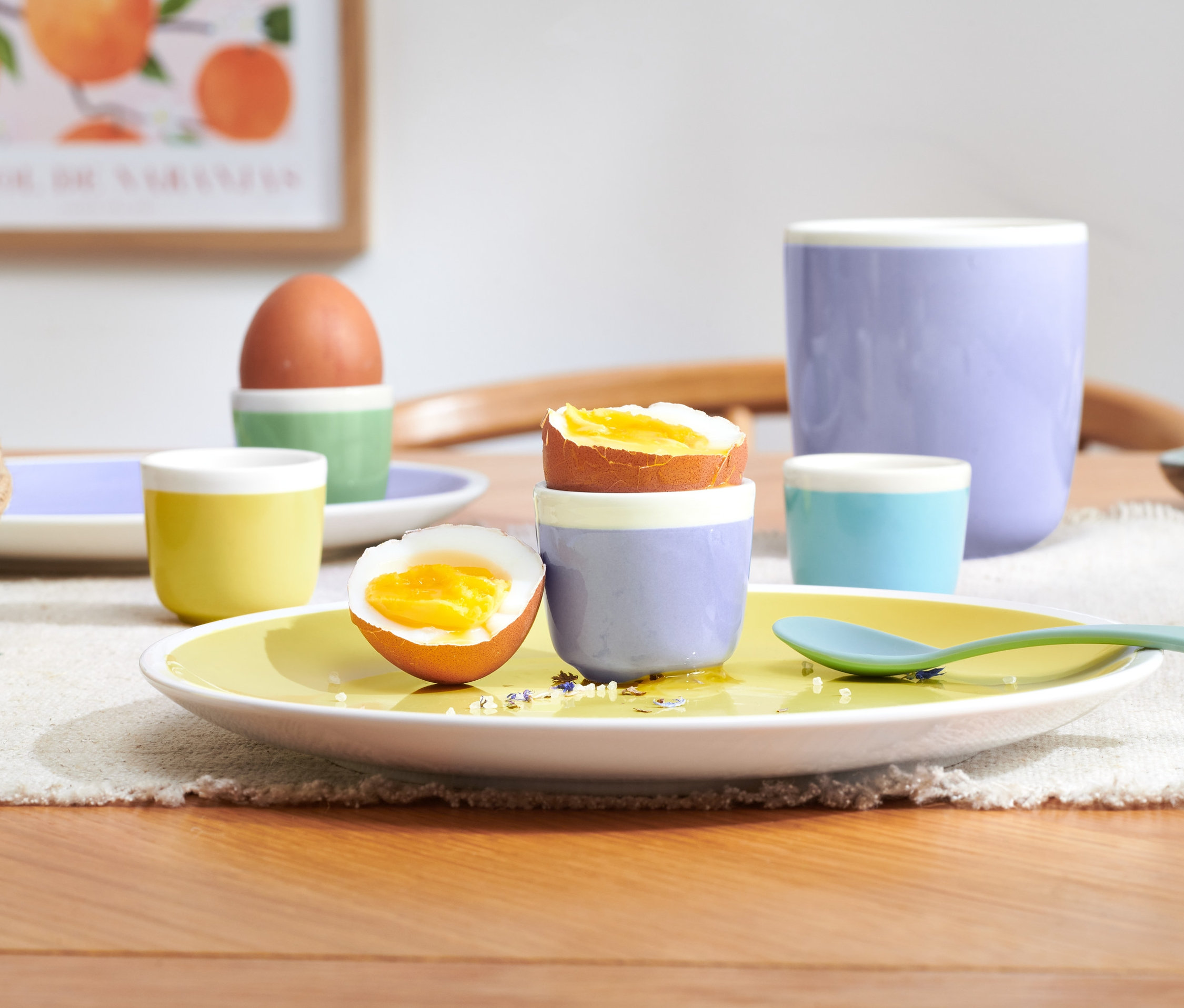 Połówka jajka w kieliszku na żółtym talerzu i 3 dodatkowe kieliszki do jajek.