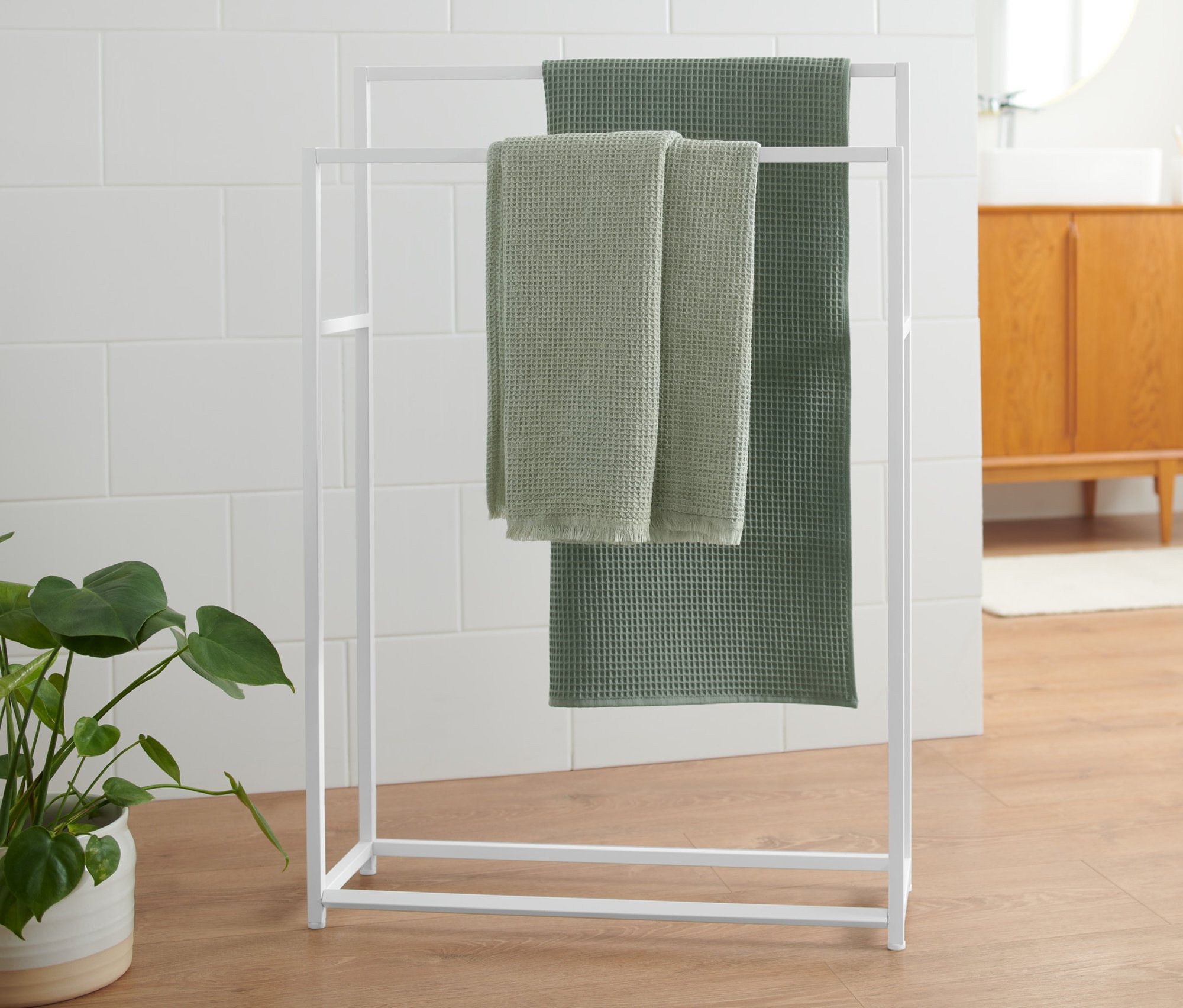 Dwa zielone ręczniki wiszą na białym wieszaku na ręczniki.