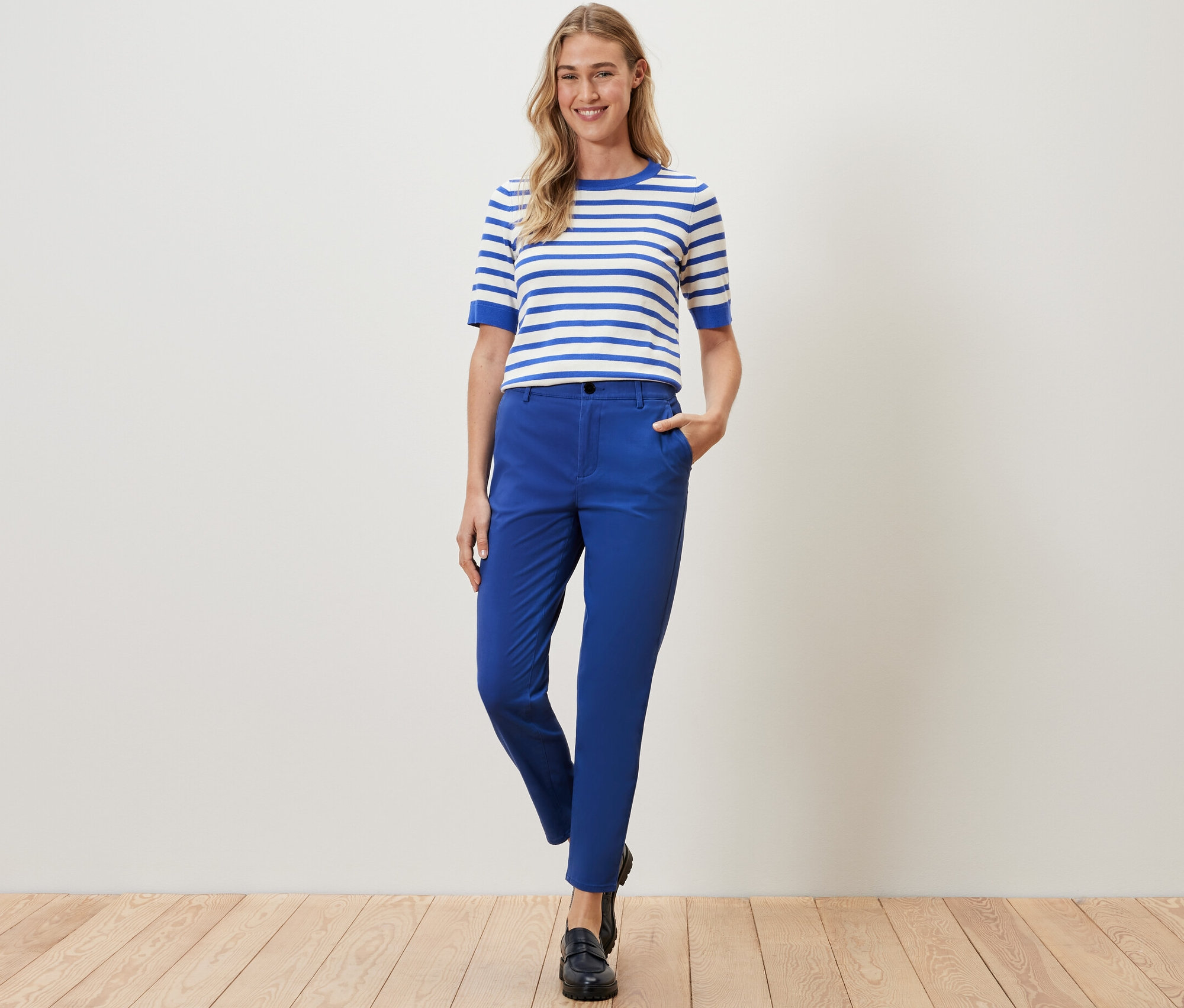 Kobieta pozuje w kobaltowych spodniach chinosach i bluzce w paski.