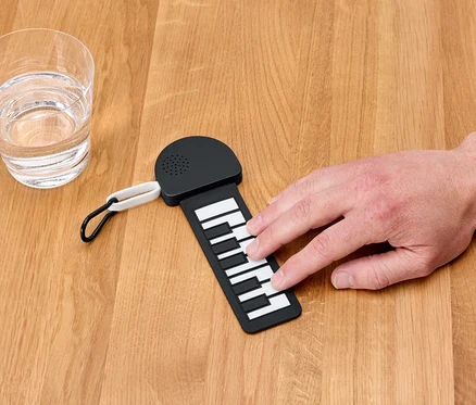 Ręka gra na mini pianinie obok szklanki wody.