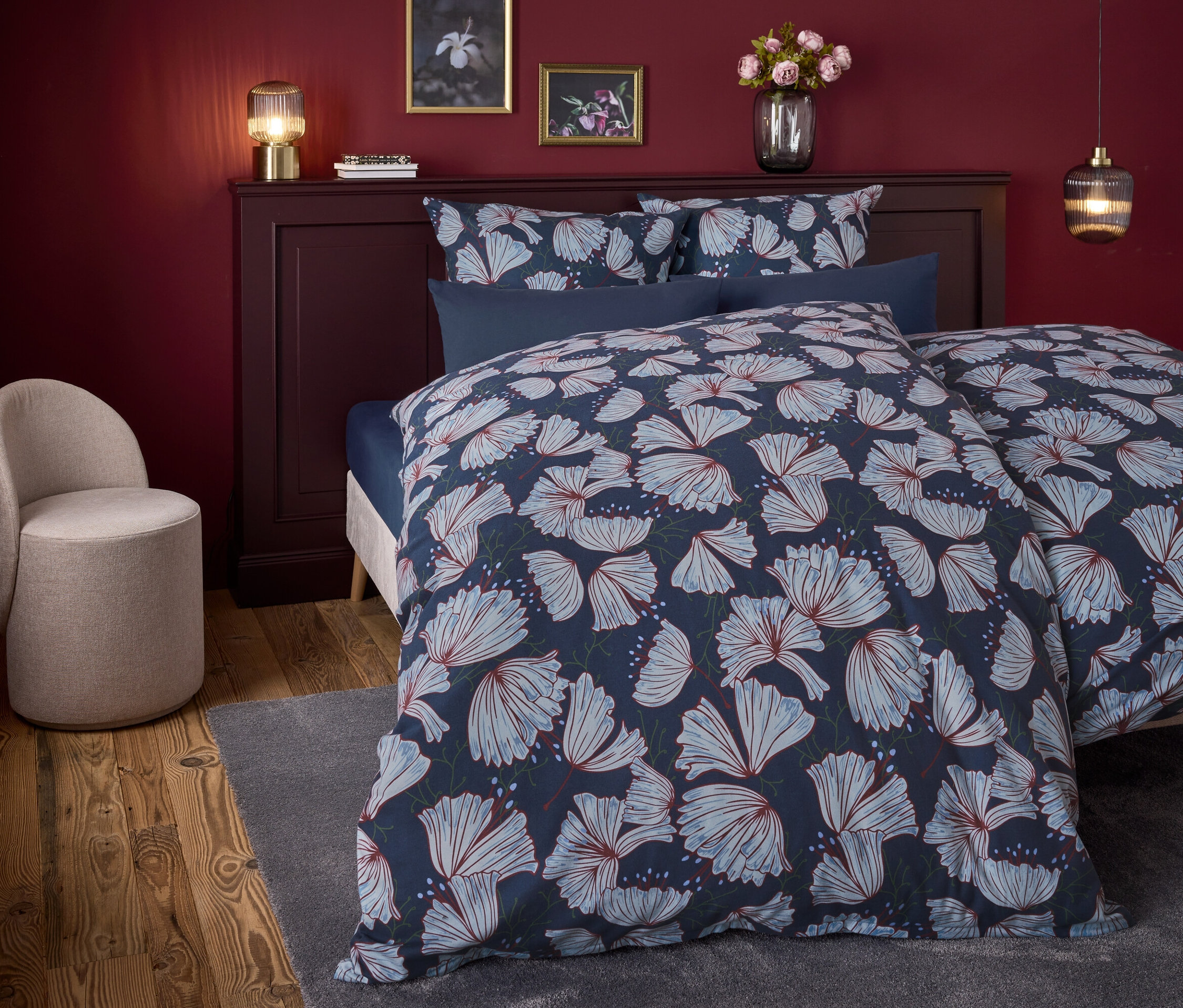 Sypialnia z łóżkiem z niebieską pościelą w kwiaty i beżowym fotelem.