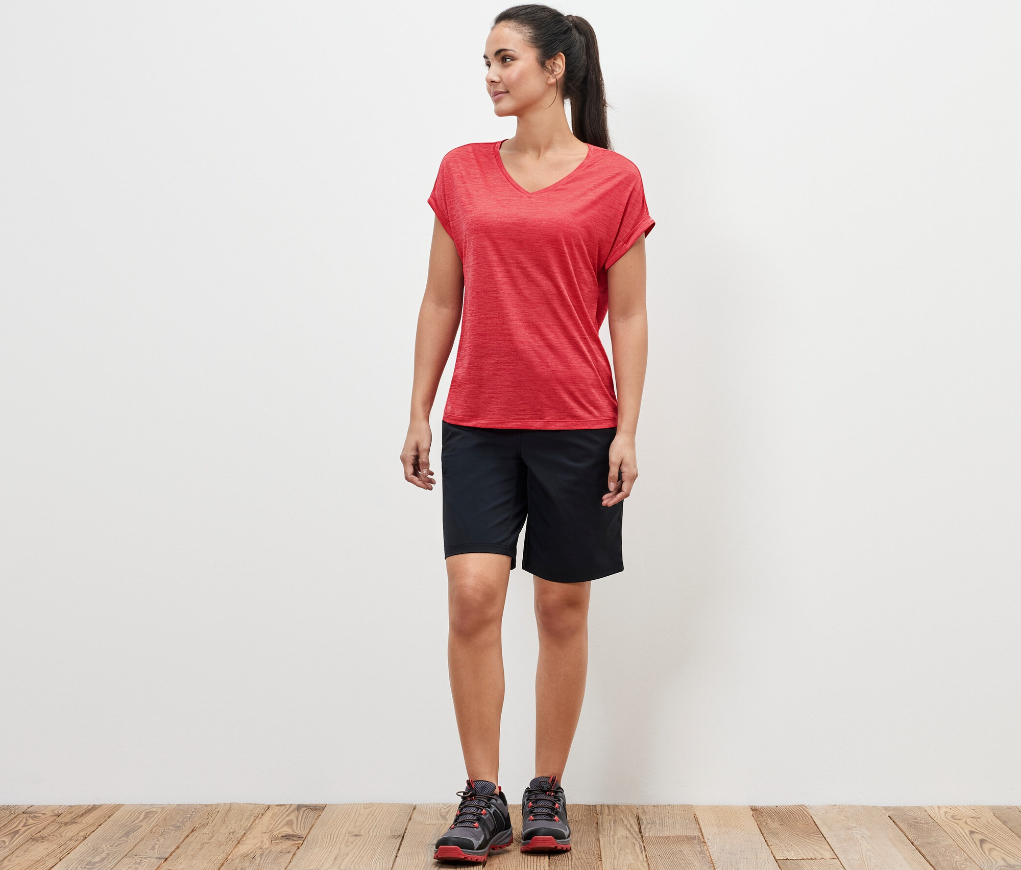 Kobieta stoi w różowej koszulce funkcyjnej i czarnych szortach.