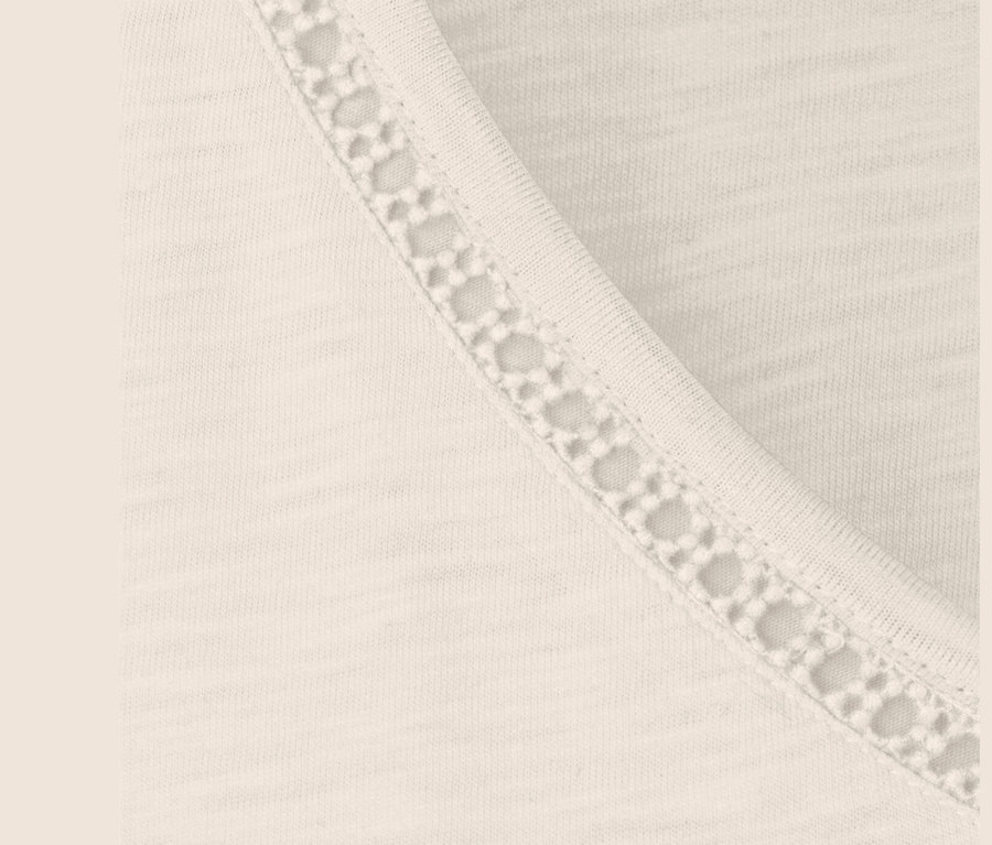Zbliżenie kremowobiałej bluzki z mieszanki modalu z koronkowym wykończeniem.