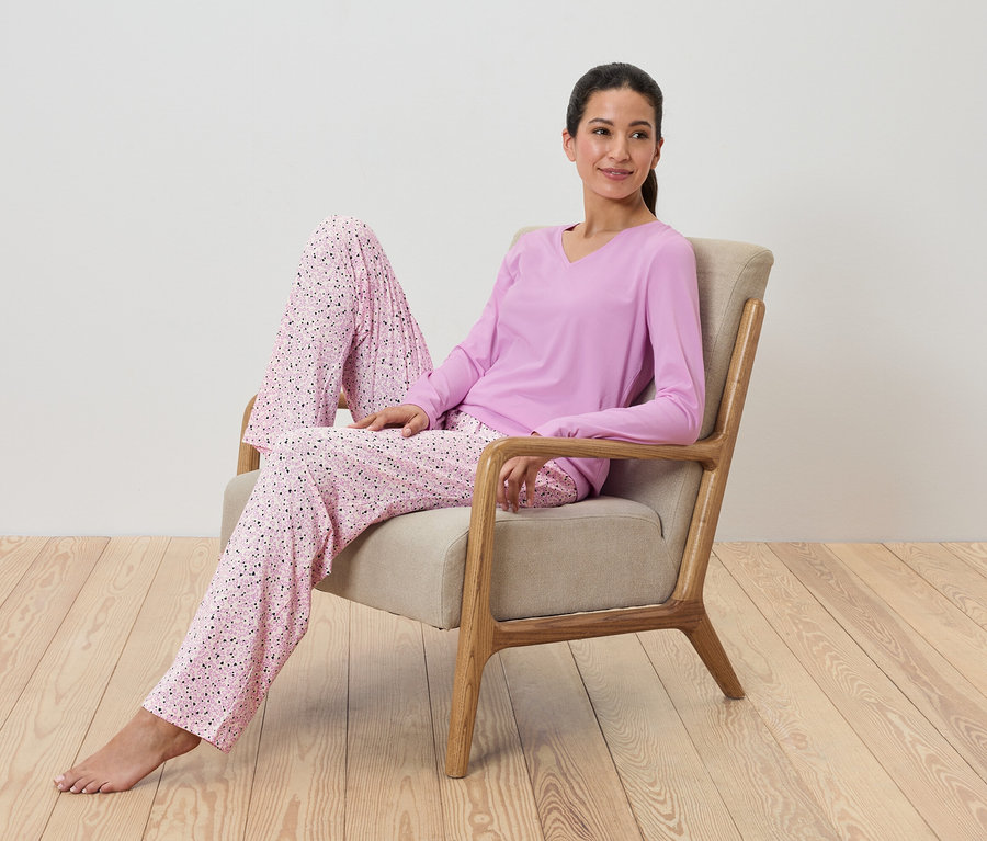 Kobieta siedzi w fotelu i ma na sobie fioletową piżamę z nadrukiem.