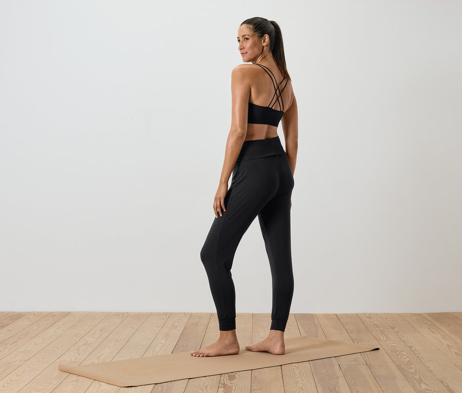 Kobieta w czarnym stroju sportowym stoi na macie do ćwiczeń.
