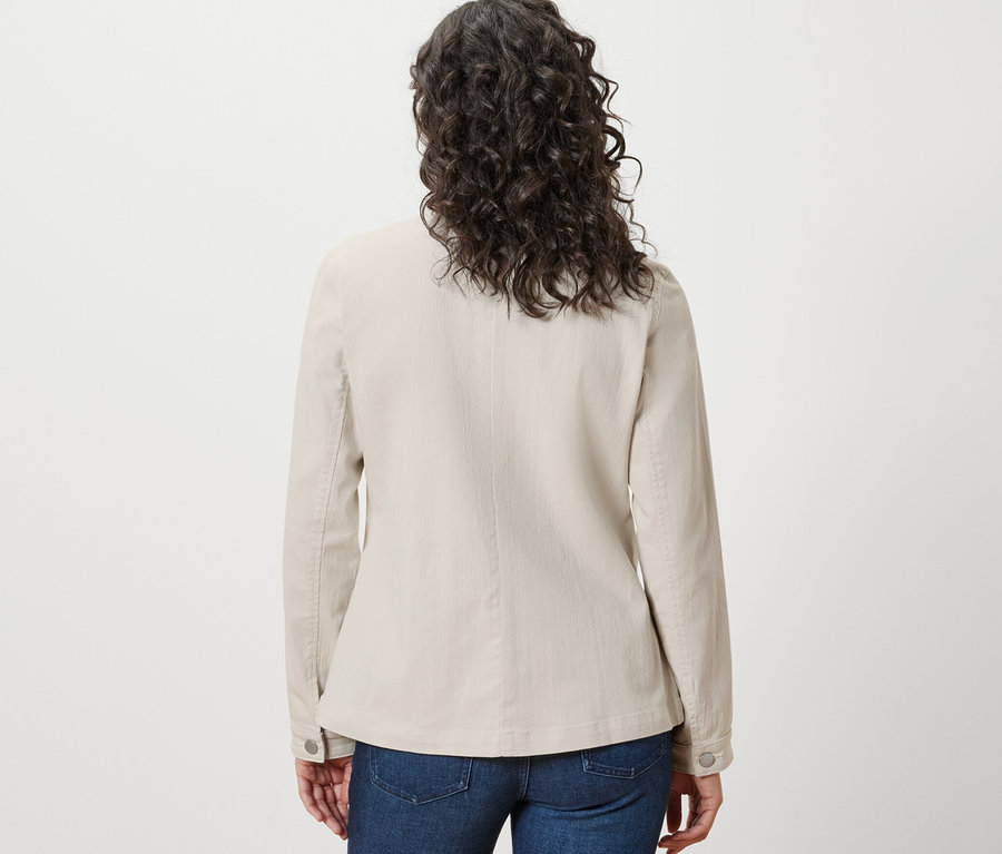 Widok z tyłu kobiety z brązowymi, falistymi włosami w kurtce dżinsowej z kieszeniami cargo i niebieskich dżinsach.