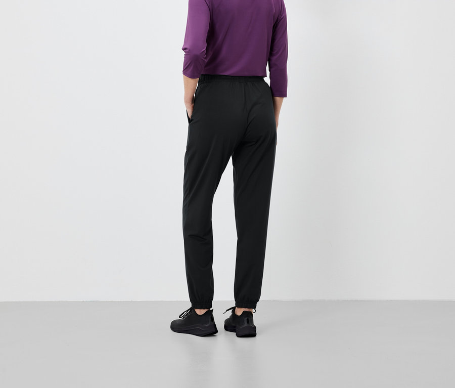 Osoba stoi tyłem, ubrana w czarne spodnie i fioletową koszulkę.