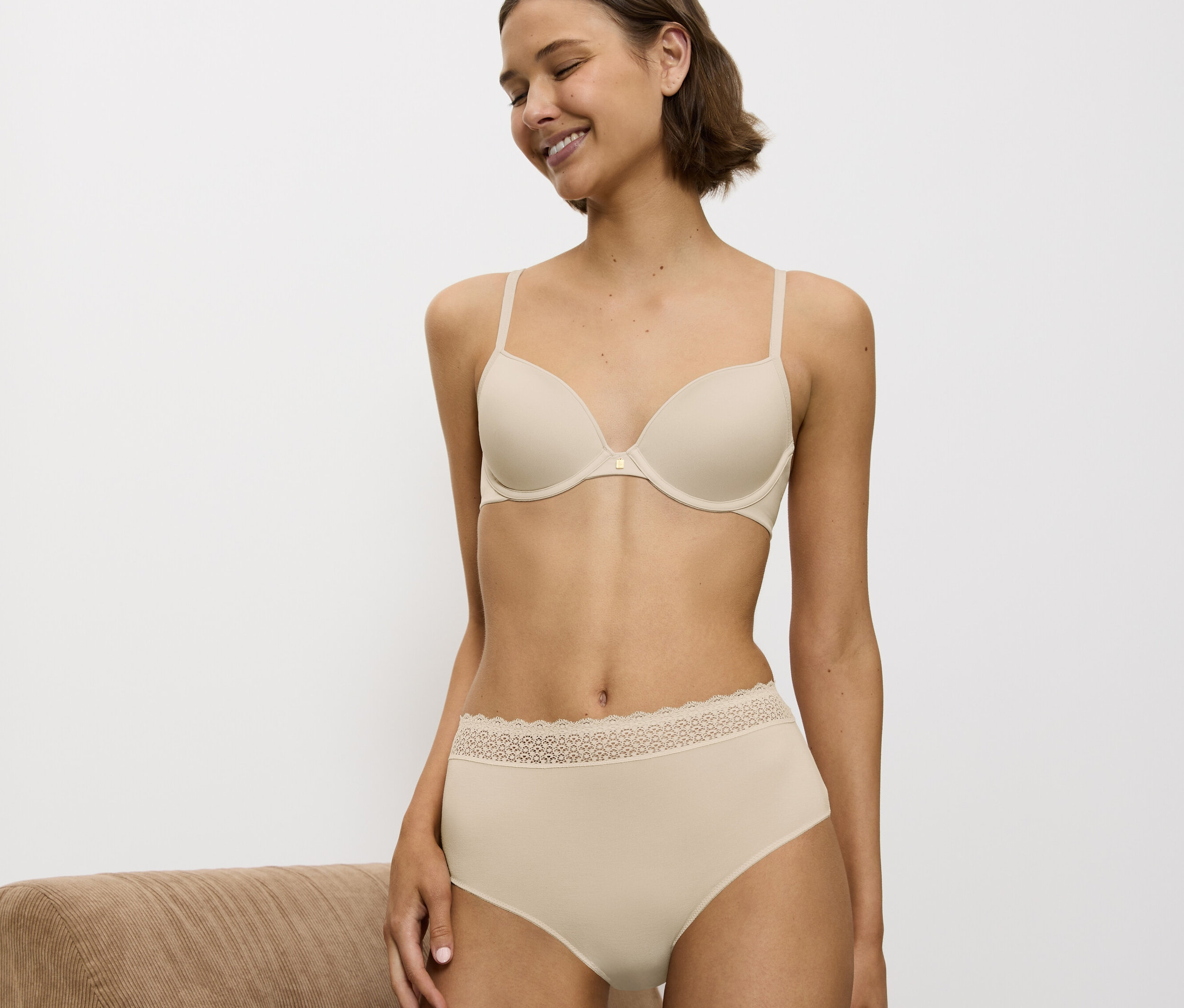 Uśmiechnięta kobieta w beżowym biustonoszu i majtkach z koronką.