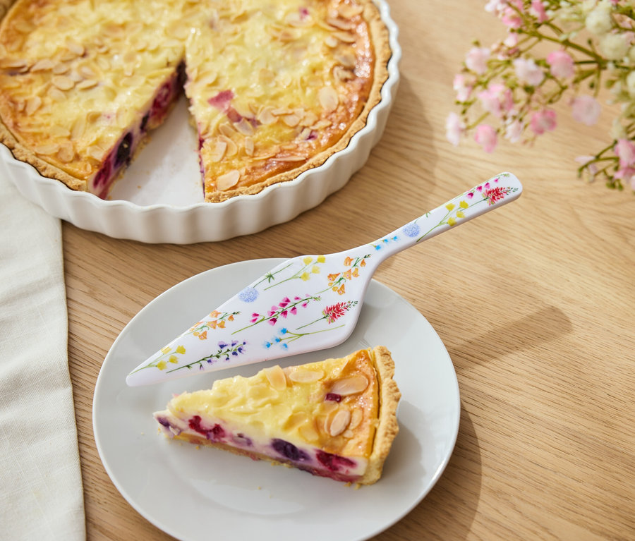 Ciasto owocowe z migdałami w białej formie, kawałek ciasta na talerzu i łopatka do ciasta w kwiaty.