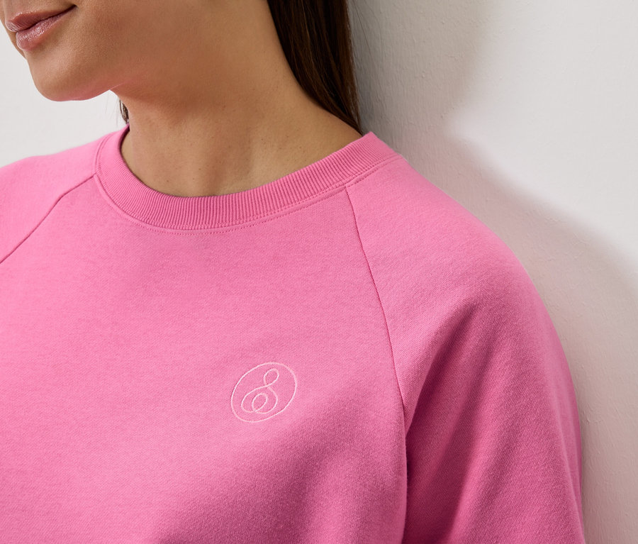 Zbliżenie na kobietę w różowej bluzie z długim rękawem i logo.