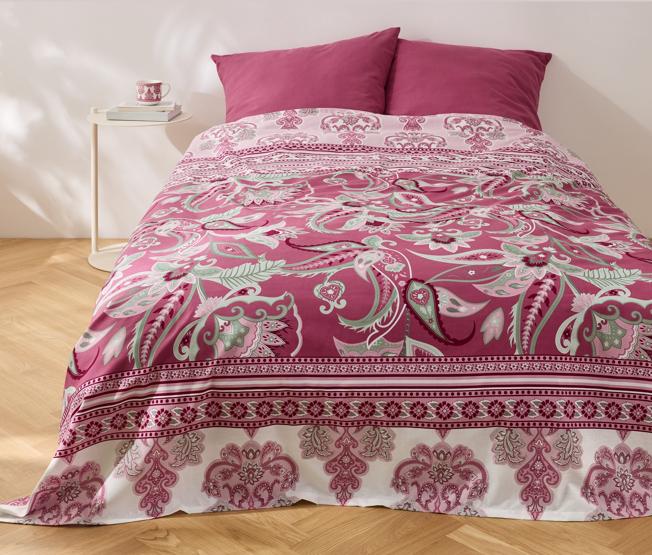 Łóżko z narzutą Renforcé-Multifunktions-Überwurf w kwiatowy wzór i dwiema poduszkami.