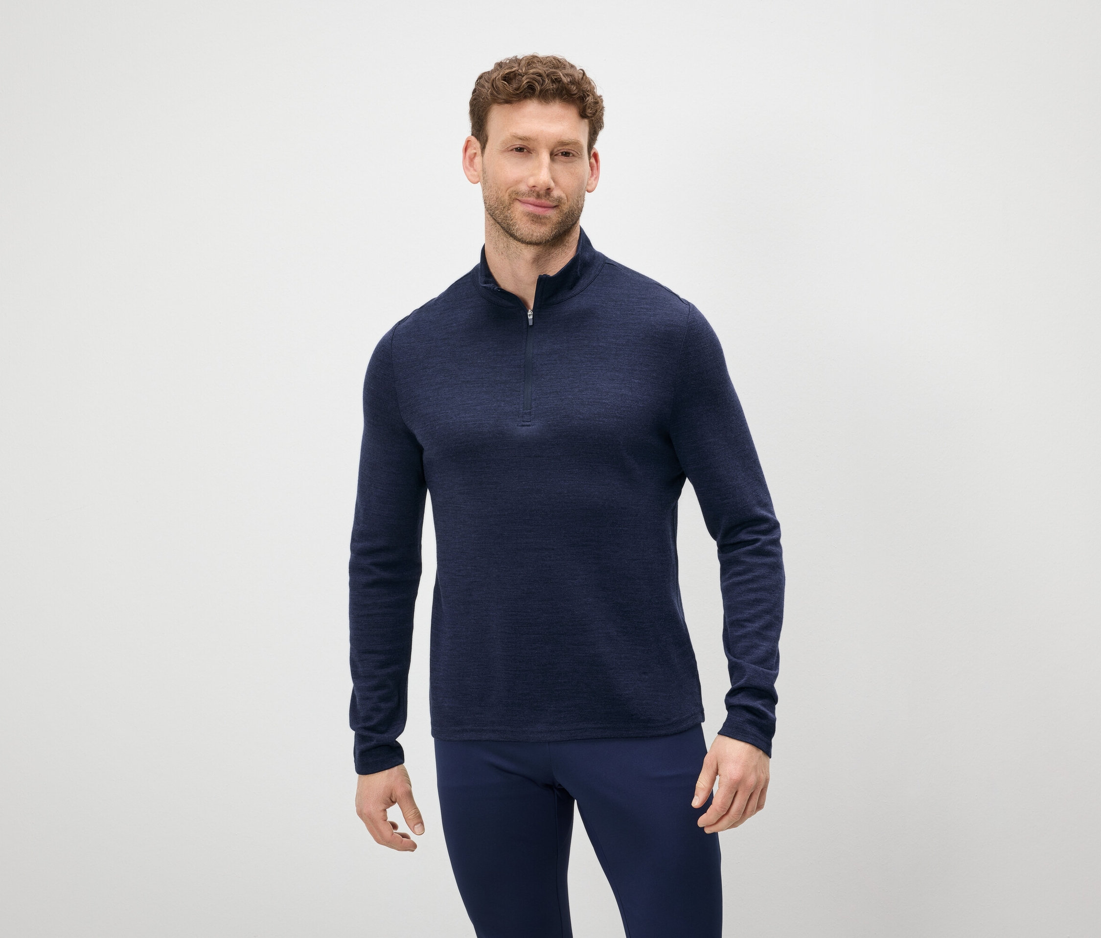 Mężczyzna z brązowymi włosami i brodą ma na sobie niebieski sweter z zamkiem błyskawicznym i niebieskie spodnie.