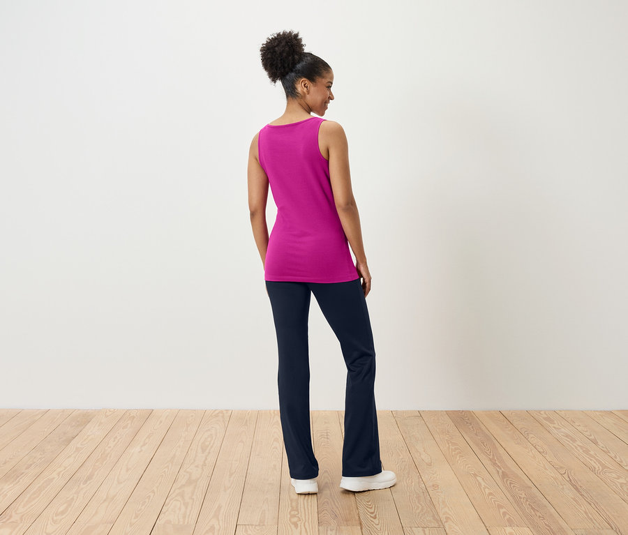 Kobieta stoi tyłem, ubrana w różowy top i granatowe spodnie.