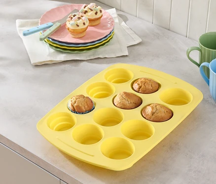 Żółta forma do muffinek z kilkoma babeczkami, talerze z babeczkami i szklanki na blacie.