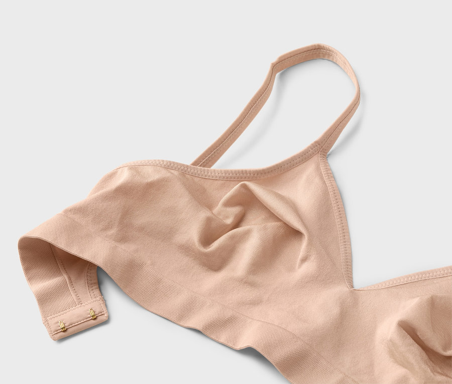 Zbliżenie beżowego biustonosza na cienkich ramiączkach ze złotymi haftkami.