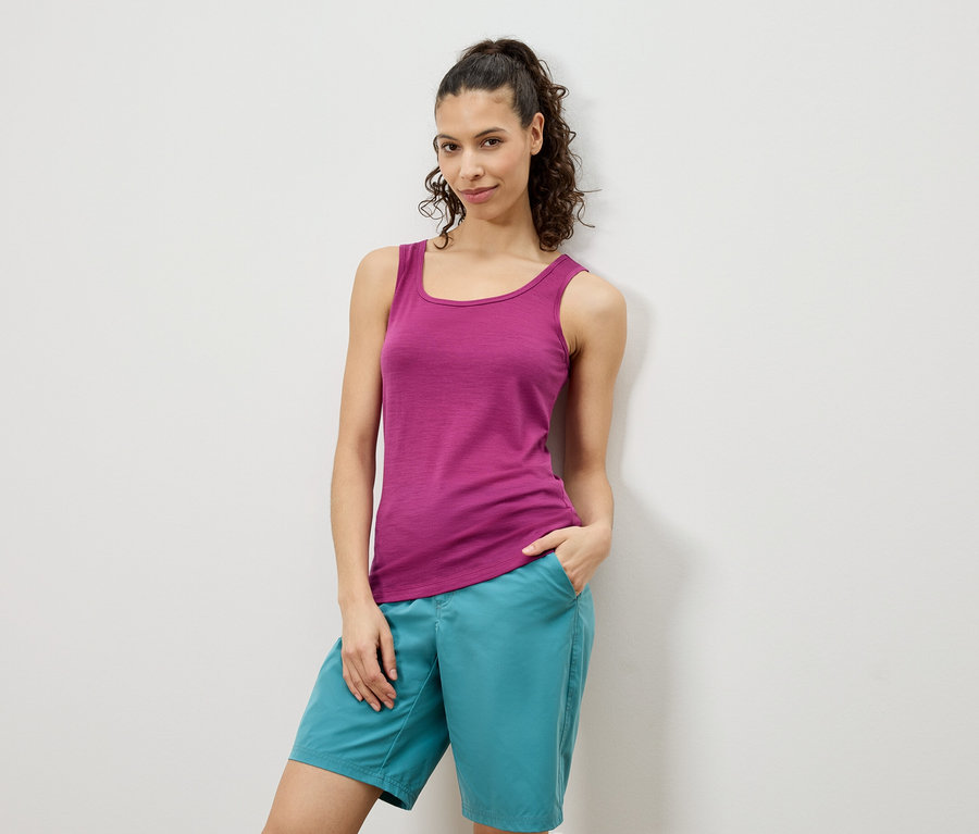 Kobieta pozuje w różowym topie na ramiączkach i turkusowych szortach na tle białej ściany.