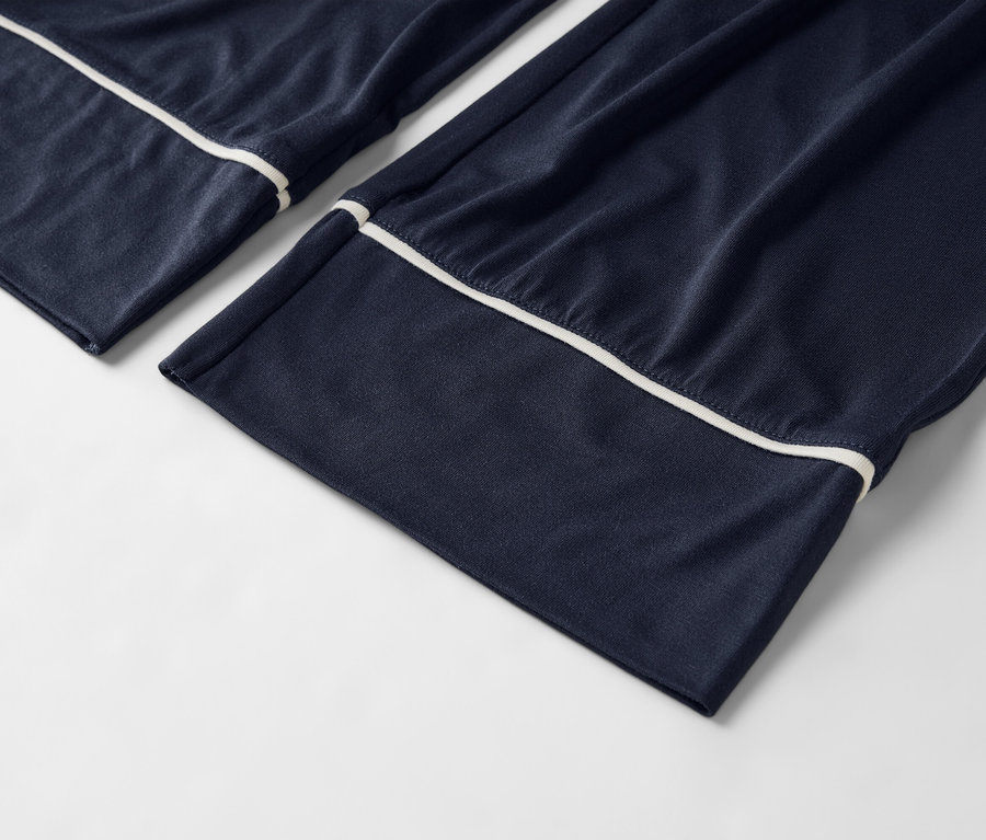 Zbliżenie granatowych spodni od piżamy z białą lamówką na białym tle.