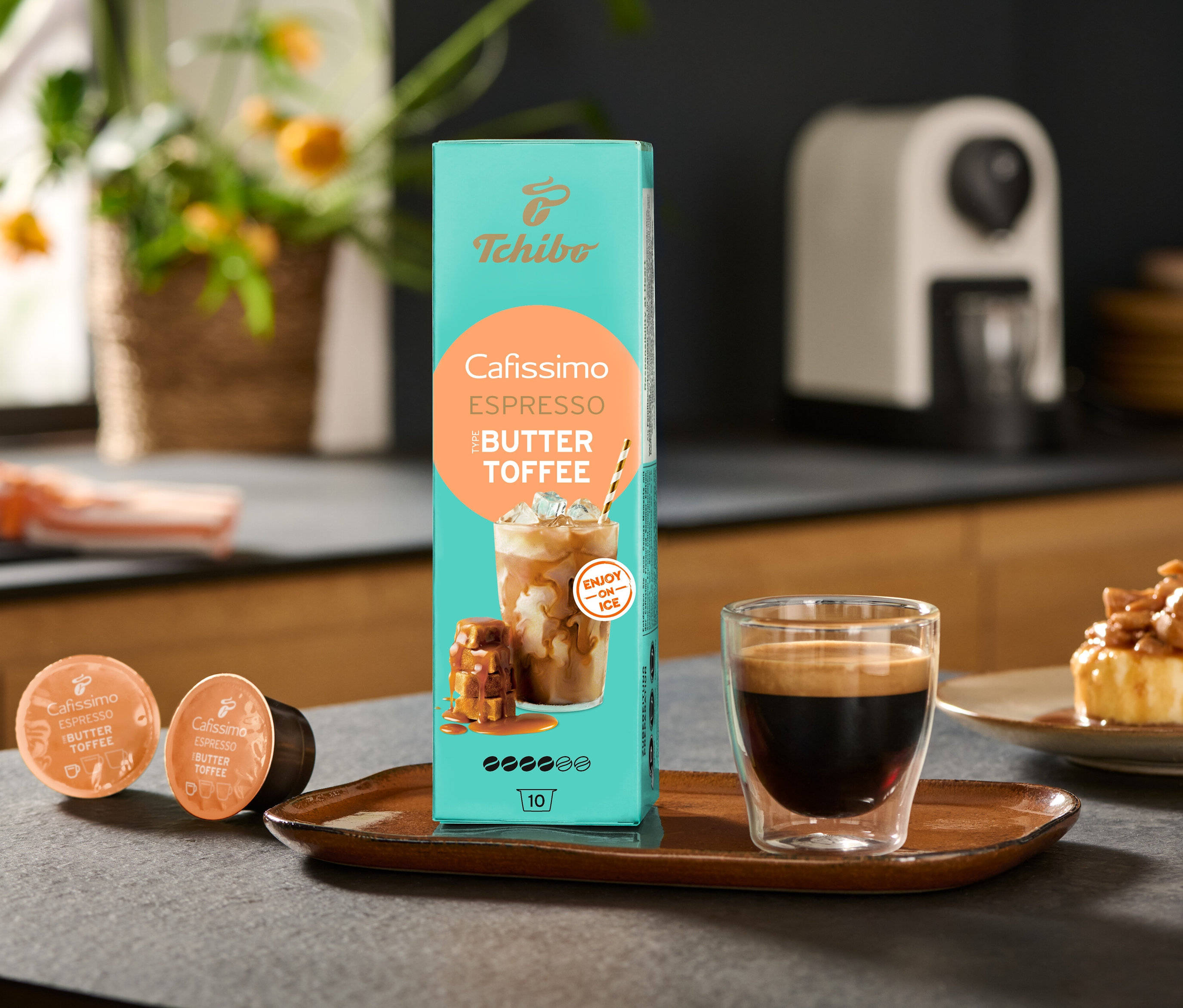 Paczka Cafissimo Flavoured Espresso – Buttertoffee i ekspres Cafissimo pure+, white stoją na stole obok filiżanki kawy.