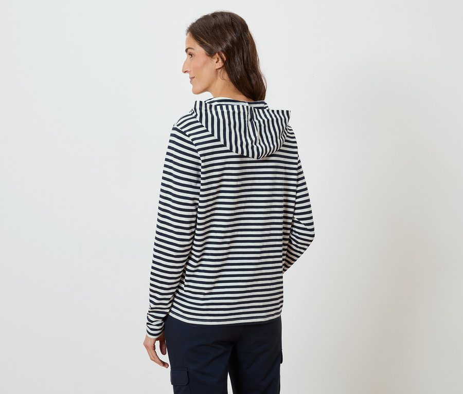 Kobieta od tyłu, ma na sobie bluzę z kapturem w paski i granatowe spodnie.