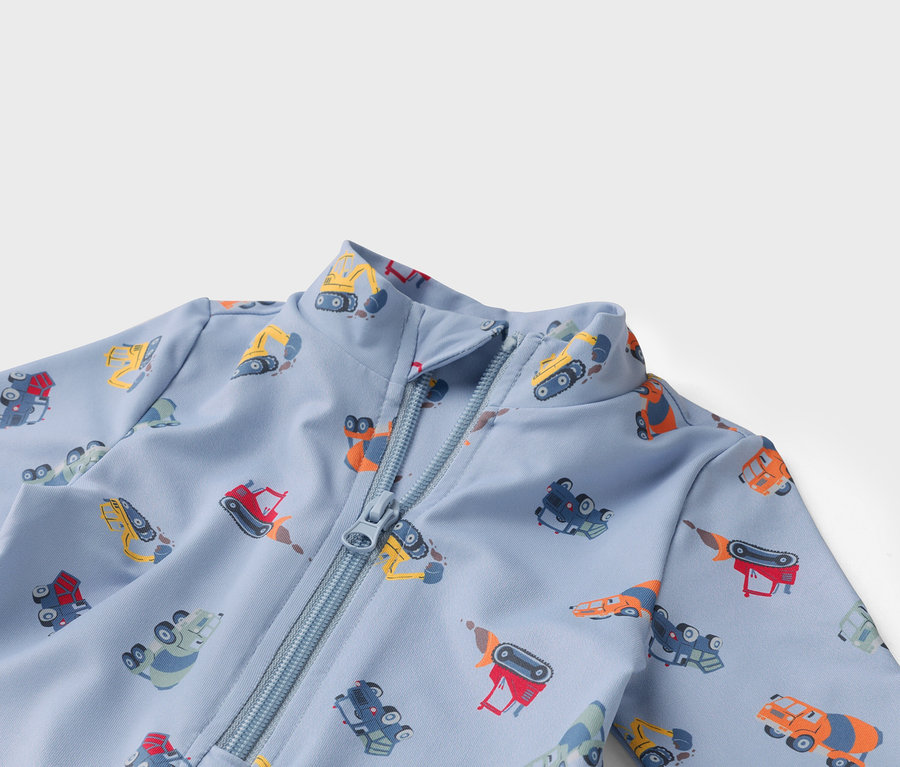 Jasnoniebieski materiał zapinany na zamek błyskawiczny z różnokolorowymi motywami wozów budowlanych.