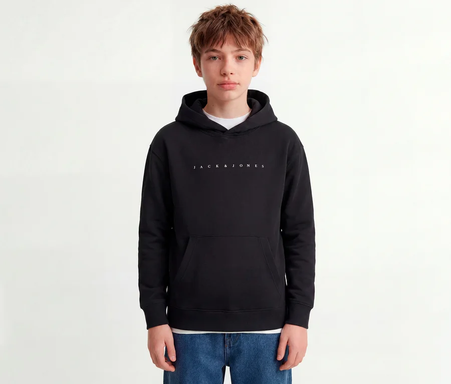Młoda osoba w czarnej bluzie z kapturem Jack&Jones Star z białym logo i niebieskich dżinsach.