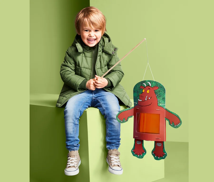 Chłopiec siedzi i trzyma w ręku lampion Gruffalo do samodzielnego złożenia.
