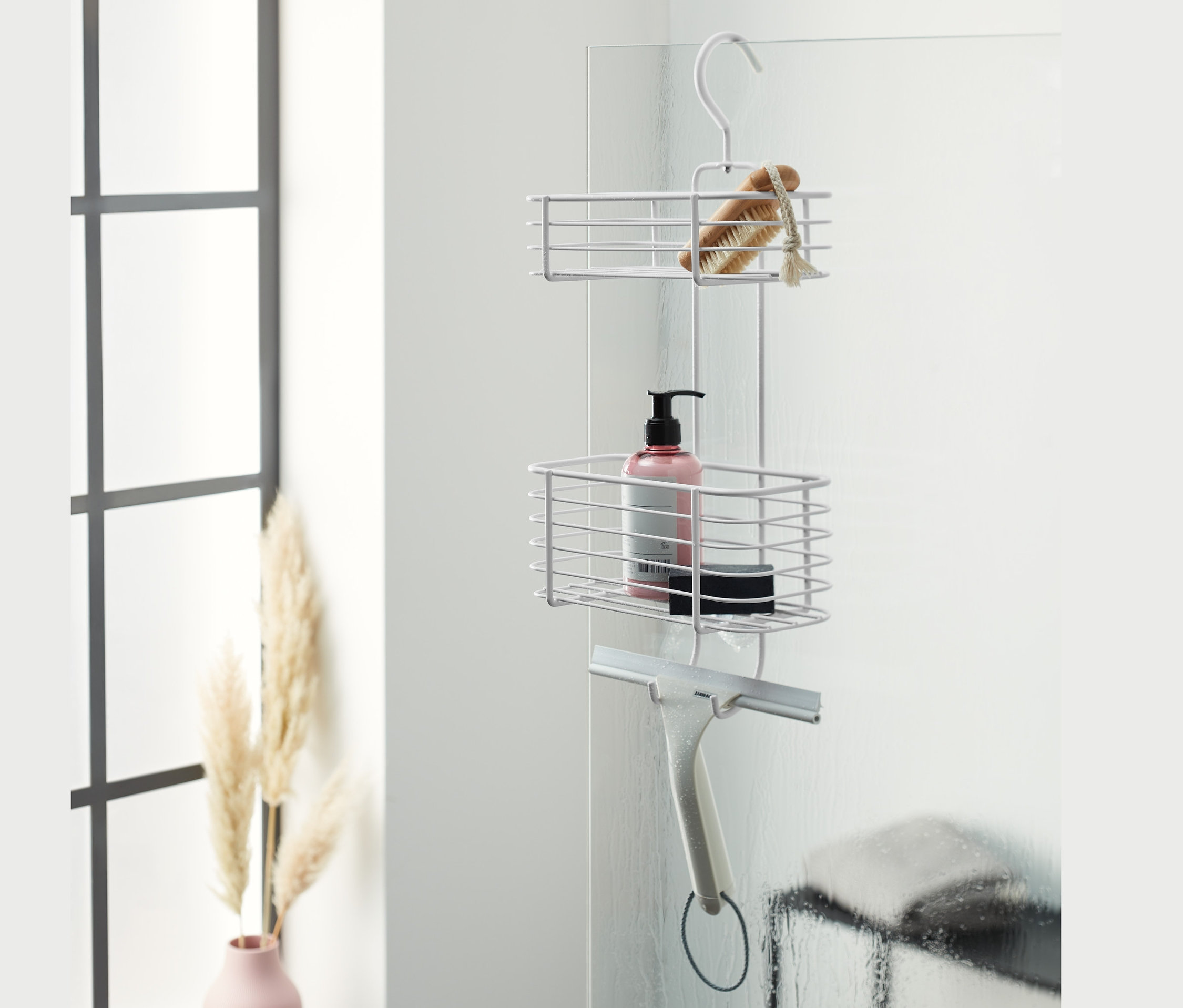 Wiszący regał pod prysznic z szczotką, butelką i ściągaczką zawieszony na ścianie prysznica.