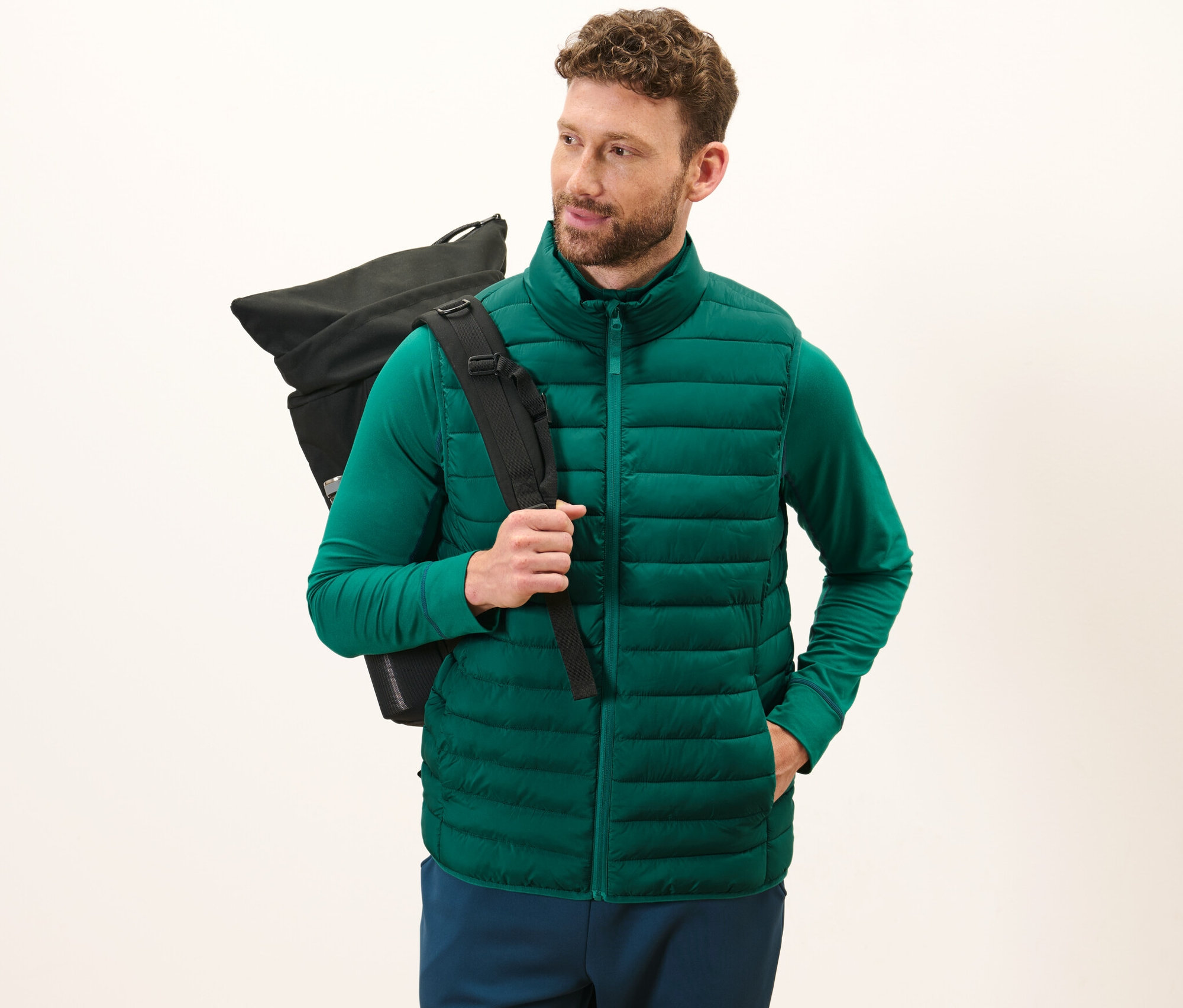 Mężczyzna ma na sobie zieloną zwijaną pikowaną kamizelkę i czarny plecak.