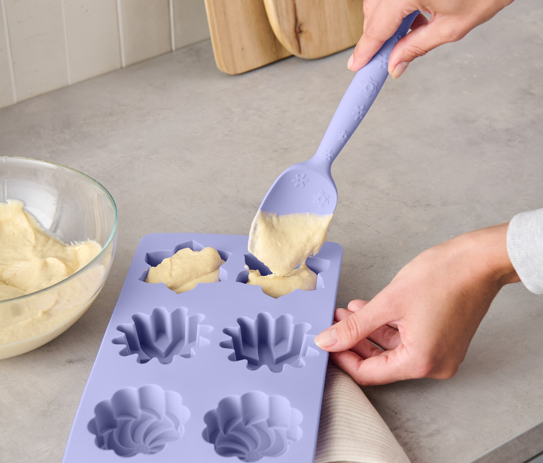 Kobieta napełnia ciasto do fioletowej silikonowej formy wielofunkcyjną łyżką do ciasta.