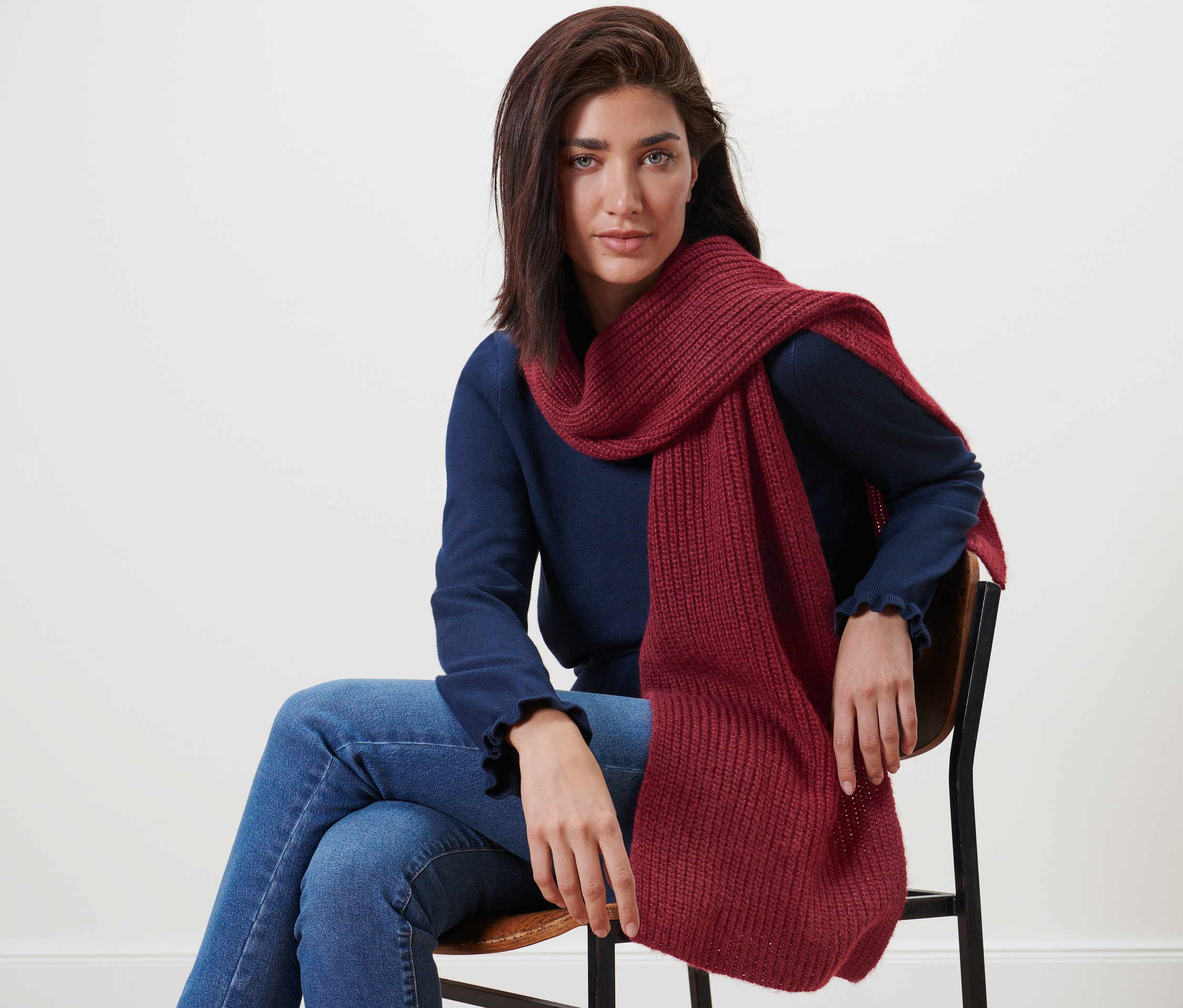 Kobieta siedzi na krześle i ma na sobie szalik z dzianiny z zawartością wełny.