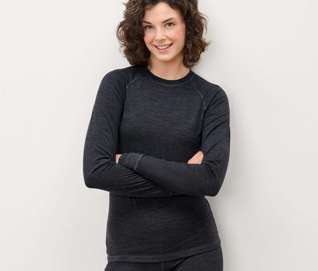 Kobieta pozuje ze skrzyżowanymi rękami w szarej koszulce funkcyjnej z wełną posiadającą certyfikat RWS i spodniach.