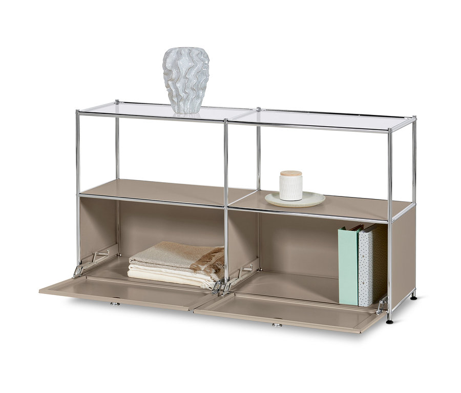 Szaro-beżowa metalowa szafka typu sideboard „CN3” z 2 klapami i szklaną półką. Na górnej półce wazon, na dolnych półkach koce i książki.