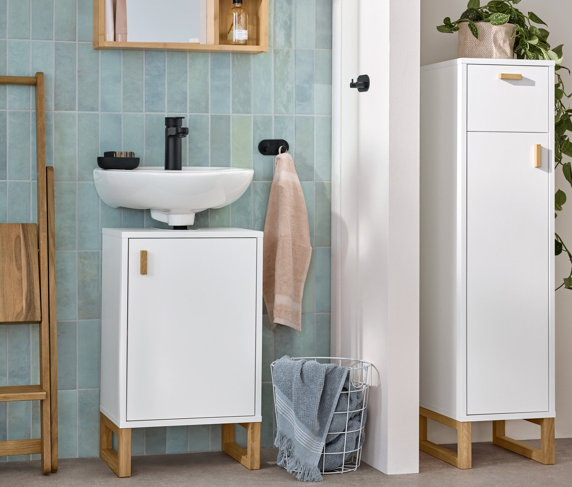 Biała łazienka z małą szafką pod umywalkę, wąską szafką łazienkową i lustrem z półkami.