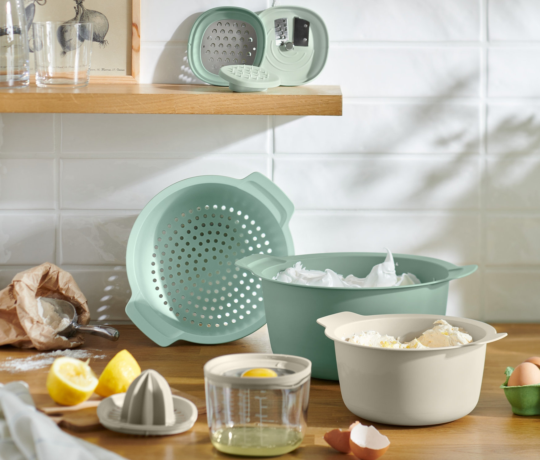 Przybory kuchenne i składniki na drewnianym blacie obejmują miskę, sitko, wyciskarkę do cytrusów, jajka i mąkę.