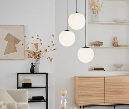 Salon z okrągłym stolikiem, szafką typu sideboard »Finnsbo« z ozdobnymi listwami, designerską konsolą ze szklanymi półkami i lampą wiszącą ze szklanymi kulami.